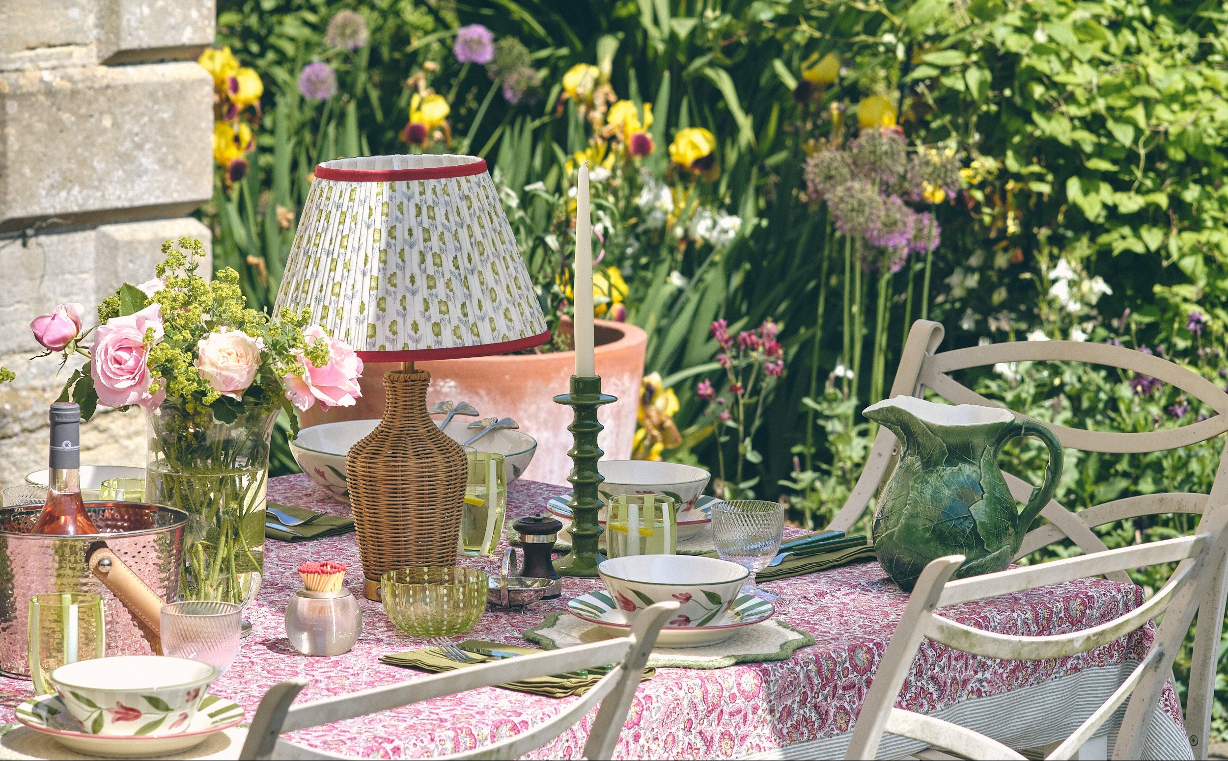 Outdoor dining table setting with floral arrangements and decorative items in a garden.