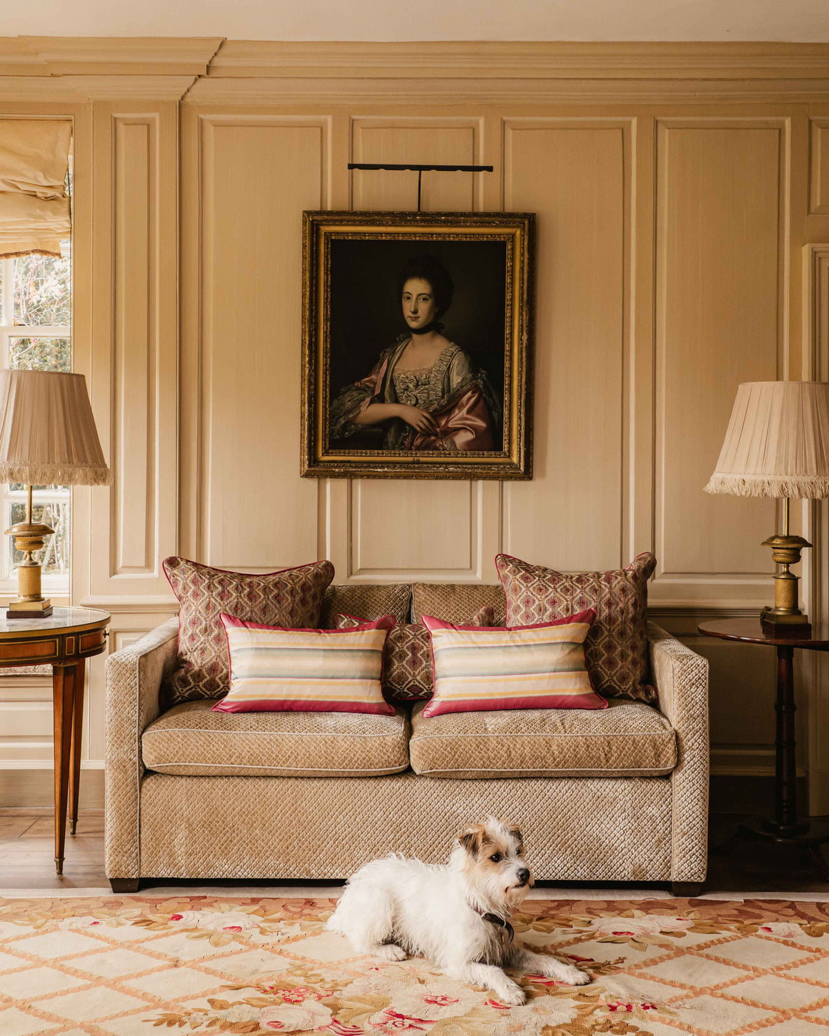 Dog lying on a patterned rug in a stylish living room with a sofa, pillows, and a portrait on the wall.