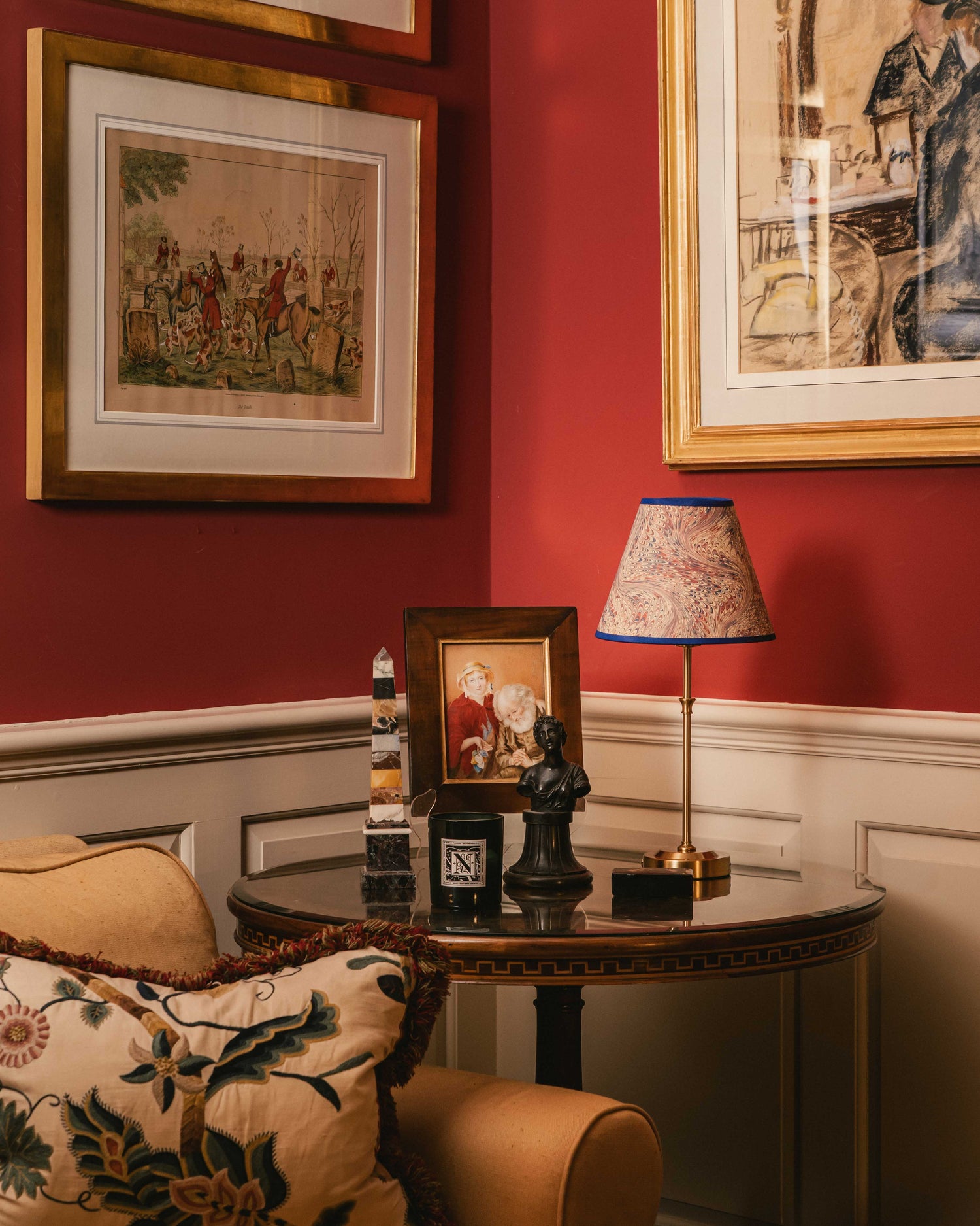 Decorative interior with a table lamp, framed pictures, and a chair against a red wall.